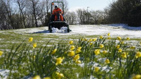 A council worker mows a lawn that has been dusted with a light covering of snow in Beamish, Durham