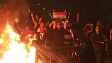 Iraqi protesters burn items to block a road during clashes with security forces