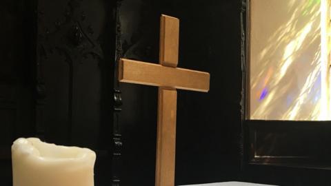 Generic image of a wooden cross and candle in a church