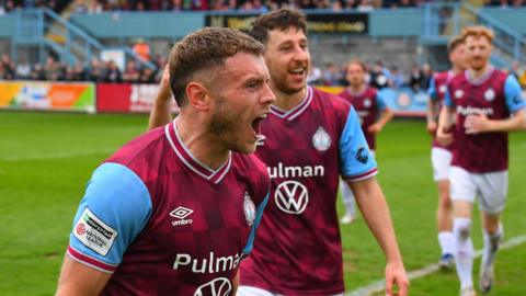 Paul Blackett celebrates after scoring a penalty as other South Shields FC players approach him. They are wearing claret and blue shirts with white shorts and socks.