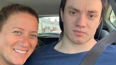 A woman and a man in a blue t-shirt sitting inside a car. 