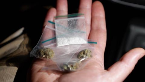 Two snap bags of what appears to be cannabis and one of what appears to be cocaine in the palm of a hand