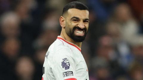 Mohamed Salah turns to his right and grimaces as he wears a white Liverpool shirt during a match at Villa Park