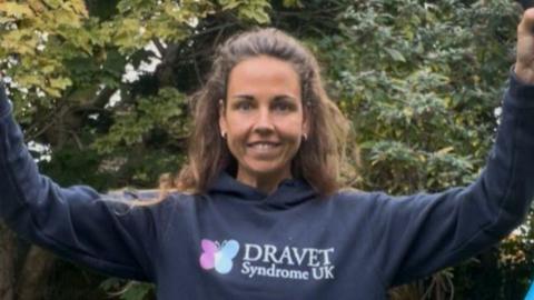 Tamara holding her arms in the air, wearing a blue Dravet Syndrome UK hoodie 