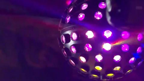 A disco ball with purple/pink and yellow lights taken in a dark room.