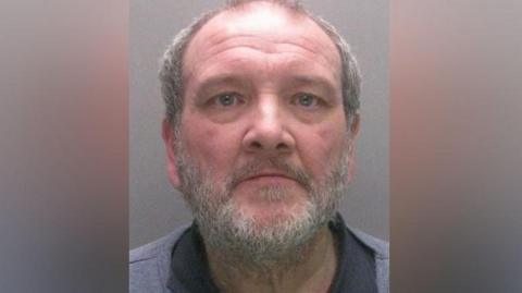 Mugshot of Douglas. He has a grey beard and thinning grey hair