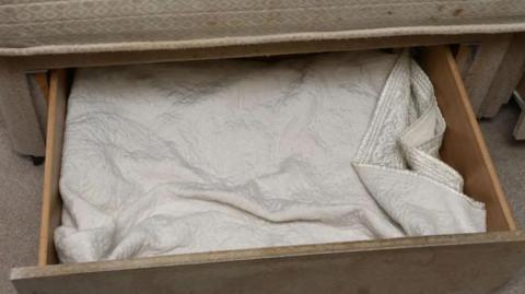 A wooden drawer in a beige bed with a cream blanket inside 