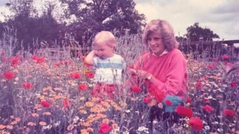 Prince William aged 2 stands in a field of flowers with his mother the late Princess of Wales