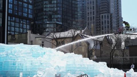Toronto Fire crews spray water on a large ice block installation created to promote rapper Drake's upcoming album.