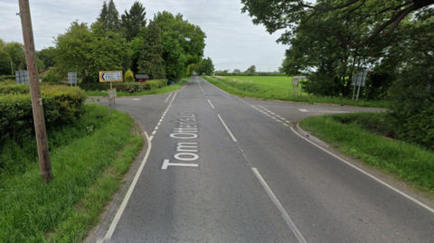 A Google Street View screen capture of the junction the crash took place near. It is a rural B road with fields and trees surrounding. 