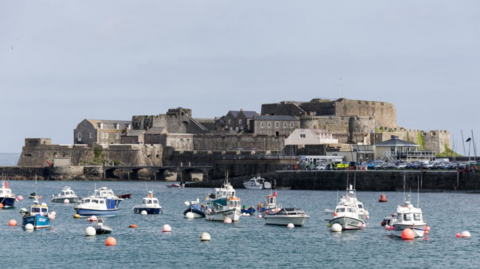 A view of Castle Cornet on an island with a number of small boats on the water in front of it.