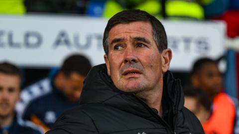 A man in his early sixties, wearing a black winter coat looking away to his right.