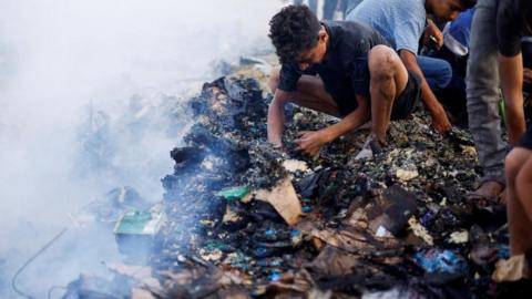 Palestinians search for food among burnt debris in the aftermath of an Israeli strike on an area designated for displaced people, in Rafah in the southern Gaza Strip, May 27, 2024.