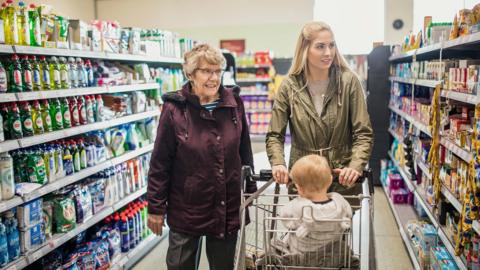 Three generations shopping in a supermarket together and smiling with a grandmother, mother and baby daugher in a shopping trolley