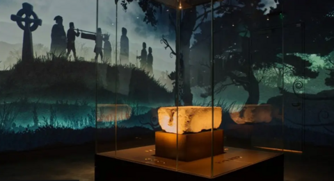 The Stone of Destiny sits in a glass case with a projected background showing silhouetted figures and a cross