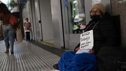 Unemployed Viviana Quevedo, 57, sits on a street holding a sign that reads "I am looking for a job in order to be able to rent" in Buenos Aires, 25 September 2024