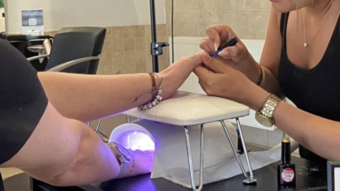 Woman has one hand under UV light and beautician holds the other hand to paint it