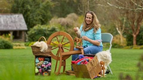 A woman uses a wool spinning wheel