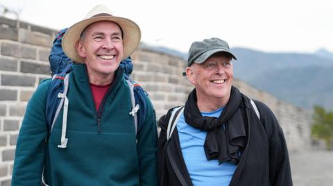 Brian Mole (left) and Melvyn Mole (right) at the Great Wall of China. They are wearing their hiking equipment including rucksacks.