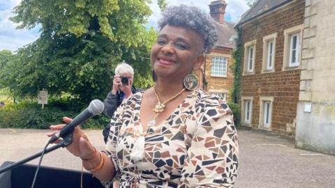 Myrle Roach holding a microphone and smiling outside