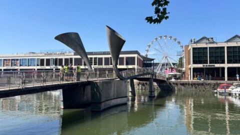 Peros' Bridge in Bristol Harbour, with the nearer section visibly higher than the far section. Workmen in high vis jackets are standing on the bridge.