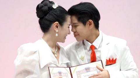 Couple with heads pressed together holding marriage certificate