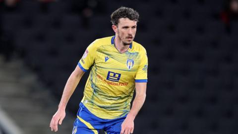 A photo of Tom Flanagan playing for Colchester United in their yellow and blue kit against former team MK Dons in March.