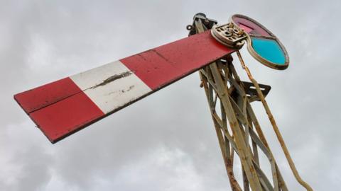 Wooden semaphore signals that were used on the railway lines. It shows a downward facing rectangle of red and white painted wood attached to a pulley and hinge