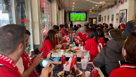 Fans wearing red jerseys watching Canada play Belgium in the FIFA World Cup on the TV in a Toronto bar.