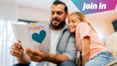 A blurred Dad and daughter are cuddled together. The Dad is holding a card which is in focus in the foreground. It says Happy Father Day with a big glittery heart in the middle