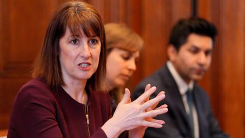 Chancellor Rachel Reeves sitting down and speaking at a meeting of industry regulators in a wood-panelled room at 10 Downing Street in London