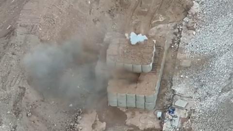 Smoke rises through dozens of giant sand bags as a bomb is detonated