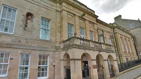 An imposing stone fronted building with archways and numerous windows