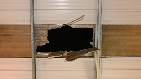 Image of a hole, taken from below, in a ceiling between two metal posts - showing damaged corrugated roofing hanging down into the opening and darkness above.