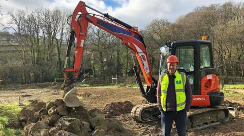 A picture of Councillor Tom Briars-Delve in front of the construction site. He is wearing a green hi-vis.