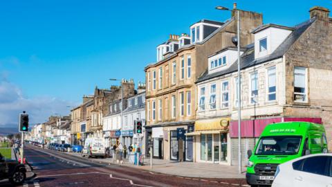 A street on a seaside town, with blue skies overhead and various shops visible