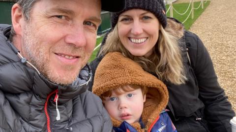 Christian and Rosie with their son Henry sitting outside a stately home