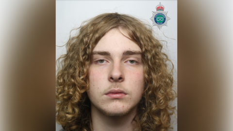 A mugshot of a boy with long curly blonde hair.
