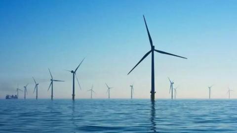 A number of wind-turbines emerging from the ocean surface against a blue sky