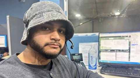 Alberto Salagan, who is wearing a hat, looks at the camera while sat at his desk