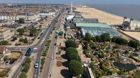 An aerial picture of Great Yarmouth taken by a drone. To the right is a sandy beach and a pier. To the left is a road with historic hotel buildings and houses stretching into the horizon