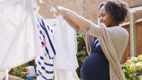 A young black pregnant woman puts washing on a washing line in a garden