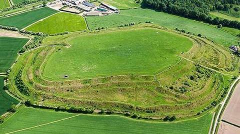 Old Oswestry, an Iron Age hillfort north of Oswestry, a raised area with ramparts, banks and ditches around it in the Shropshire countryside under a blue sky.