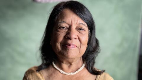 Indu Sharma smiling at the camera wearing a white necklace and light brown saree