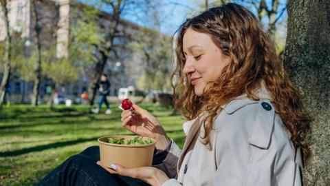 Young woman with curly hair enjoys a healthy lunch in a city park, savoring each bite in the sunshine
