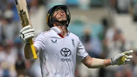 England's Matthew Fisher raises his bat and looks to the sky after hitting a fifty