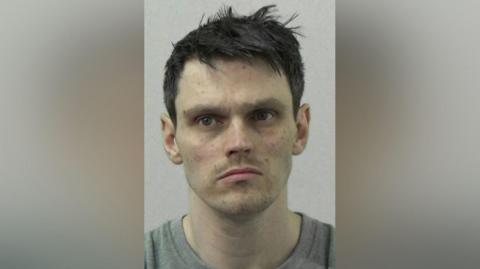 Mugshot of Warren Jackson. He has pale freckled skin and is clean shaven with short spiky black hair.