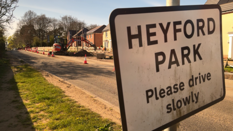 A sign of Heyford Park in Oxfordshire with a digger in the background.