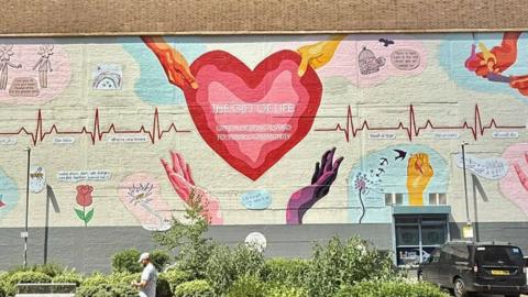 The finished mural which has a large red heart at its centre, held from above by two hands and with the words The Gift of Life inside it.