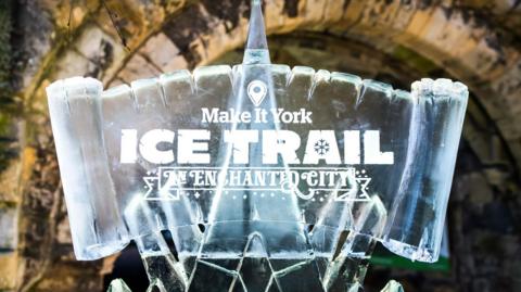 A sign carved from ice with the words Make it York Ice Trail An Enchanted City carved into the sign